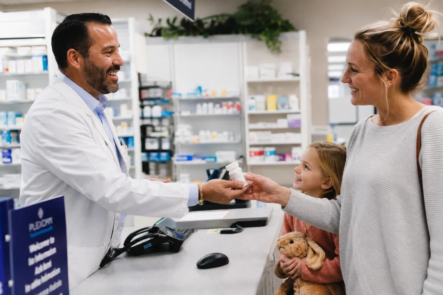 Pharmacist handing a flavored liquid medication to a smiling mother and daughter at UnityRX Pharmacy